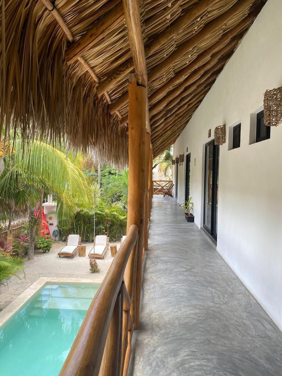 A covered outdoor area with a pool, lounge chairs, and a thatched roof.