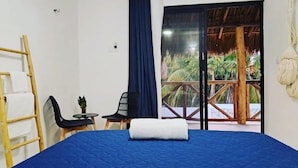 A room with a bed, a small table with a chair, a ladder, and a view of a wooden deck with plants. - Casa Baloo (El Cuyo)