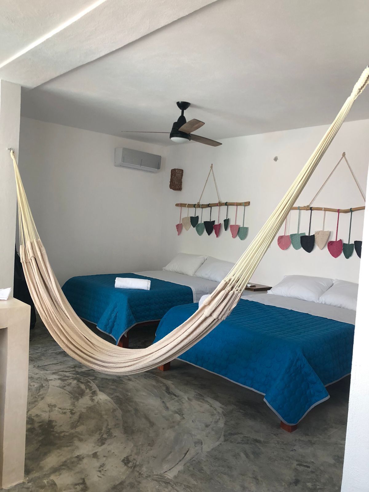 A room with two beds, a hammock, a ceiling fan, and a wall-mounted decoration.