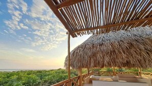 A thatched-roof structure with a wooden railing overlooking a lush green landscape and the sea. - Casa Baloo (El Cuyo)