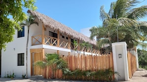 A two-story building with a thatched roof, a wooden balcony, and a bamboo fence. - Casa Baloo (El Cuyo)