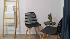 A small room with a wooden ladder, two black chairs, a small round table with a plant, and a blue curtain. - Casa Baloo (El Cuyo)