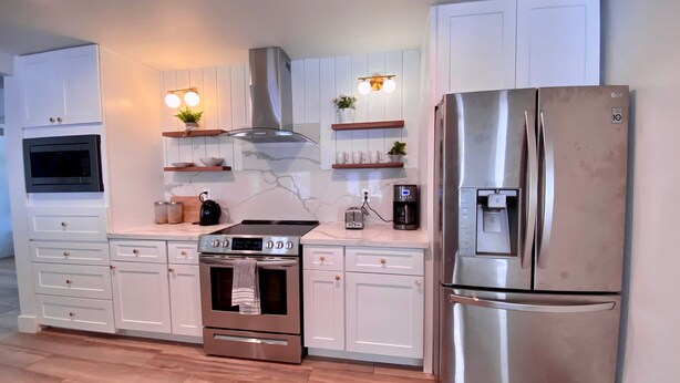 A modern kitchen with white cabinets, a stainless steel refrigerator, a built-in oven, a microwave, a coffee maker, and a toaster. - Newly Remodeled Beauty in Phoenix (Phoenix)