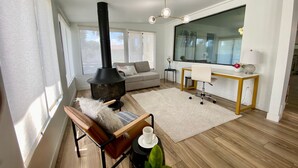 A cozy living room with a wood-burning stove, a sofa, a desk, and a large window. - Newly Remodeled Beauty in Phoenix (Phoenix)