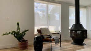 A modern living room with a black wood-burning stove, a potted fern, a wicker basket, and a chair with a throw blanket. - Newly Remodeled Beauty in Phoenix (Phoenix)