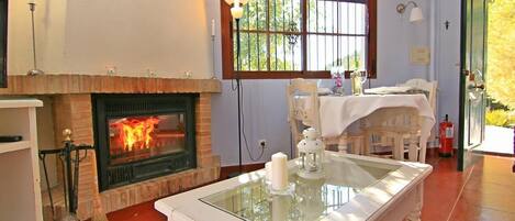 Una habitación con chimenea, una mesa de comedor y un ventanal con cortinas rojas.