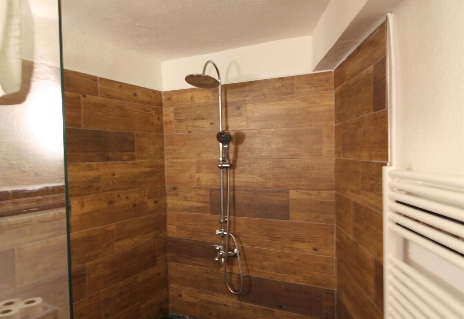 Une douche avec une porte en verre, des murs en bois et un radiateur blanc.