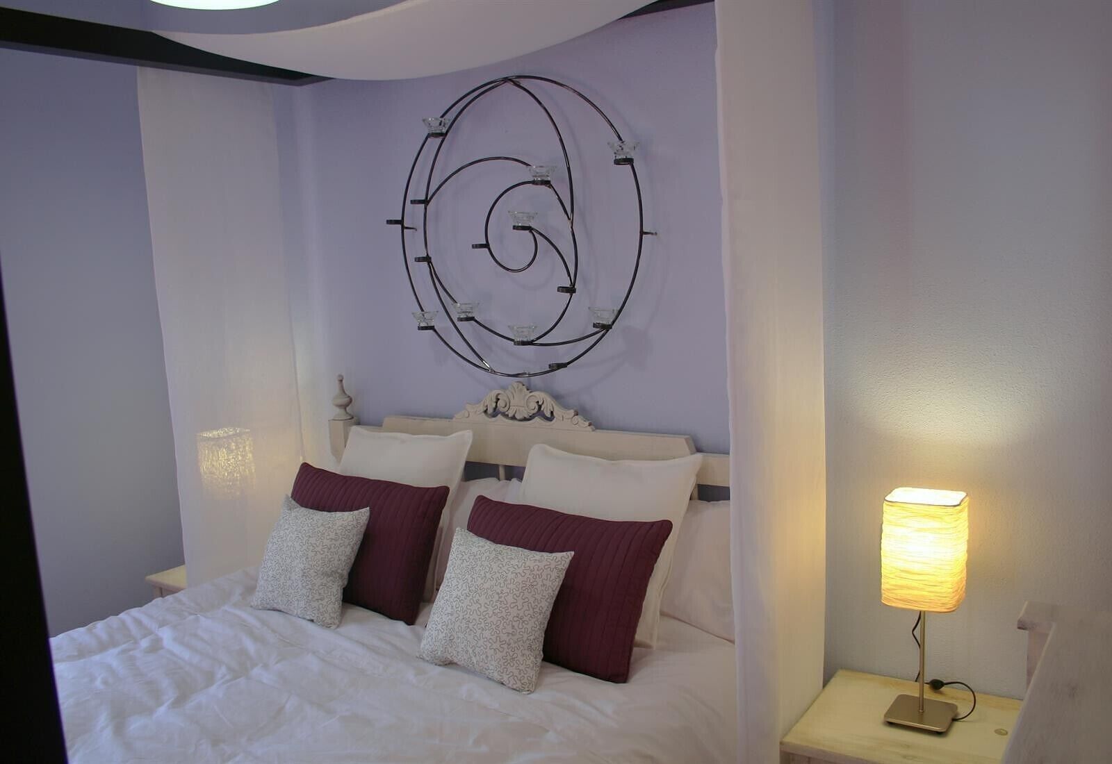A bed with white bedding and two pillows, a wall-mounted light fixture, and a bedside table with a lamp.
