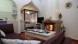 Un salon chaleureux avec une cheminée, un coin repas et une cuisine visible à travers une arche.
