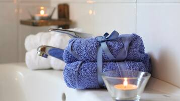 Een badkamer met een bad, een handdoekrek met handdoeken en een brandende kaars.