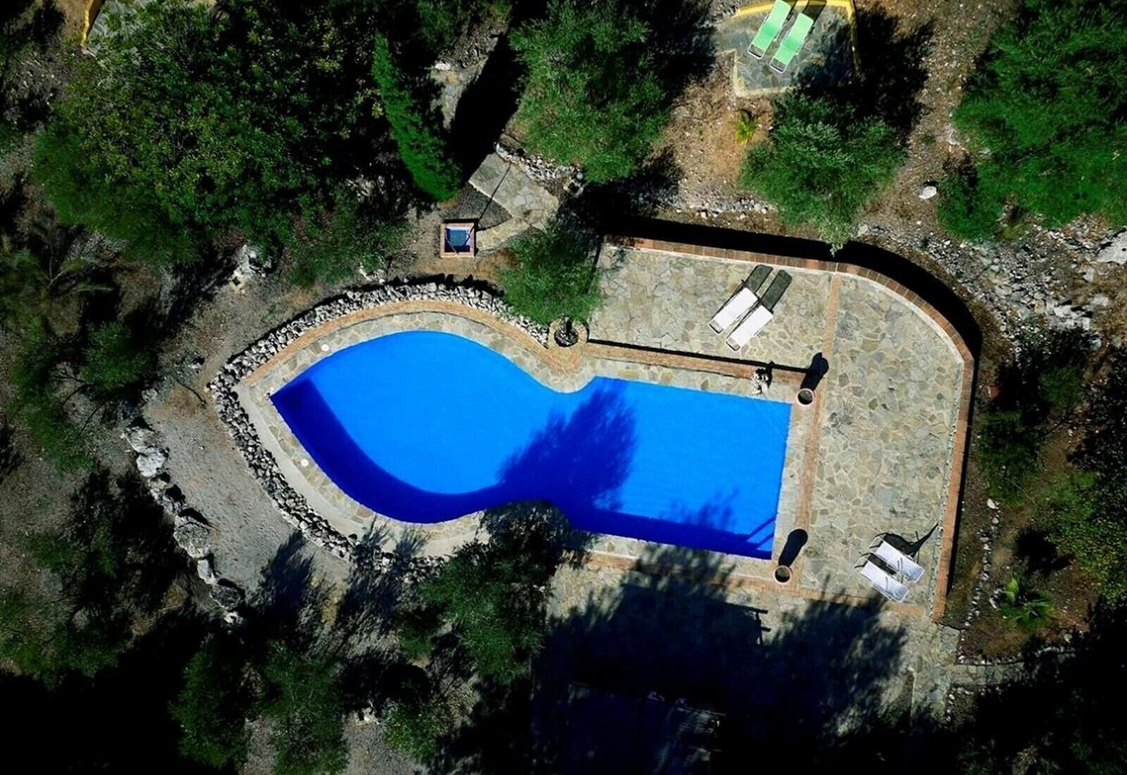 Vista aérea de una piscina rodeada por un muro de piedra, con un edificio pequeño y una zona pavimentada cerca.