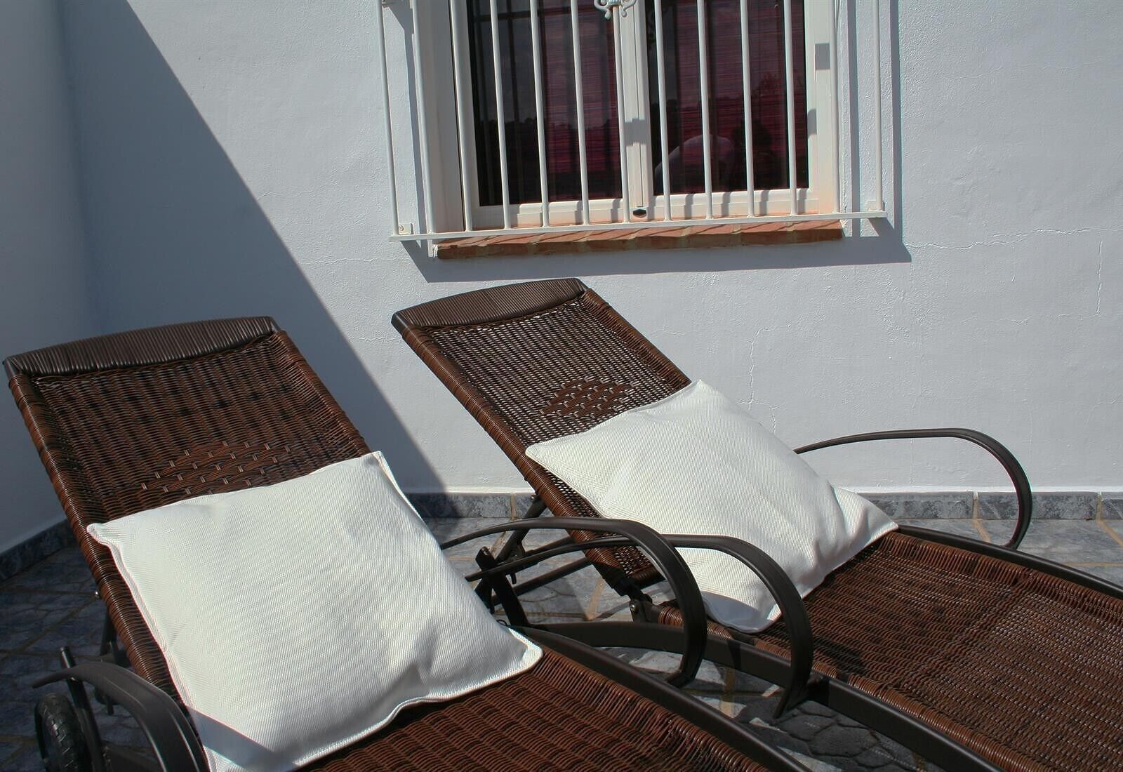 Duas cadeiras de vime com almofadas brancas, dispostas numa área de pátio com piso de azulejos.