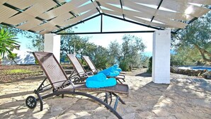 Un espace extérieur aménagé, abrité et doté de fauteuils de jardin en osier, avec une piscine en arrière-plan.