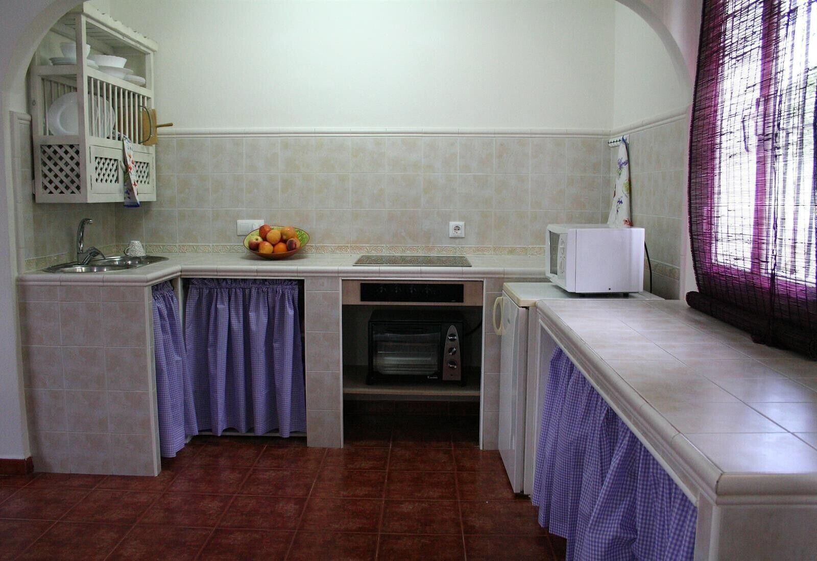 Cocina compacta con un lavamanos, microondas y un bol de frutas en la encimera.