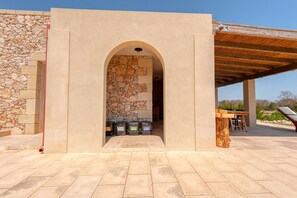Un espace extérieur abrité, doté d’une entrée avec un mur en pierre, d’une table en bois et offrant une vue sur le paysage environnant.