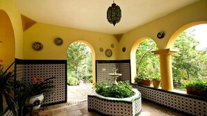 Un pati il·luminat pel sol amb parets de rajola, una font i plantes en testos.