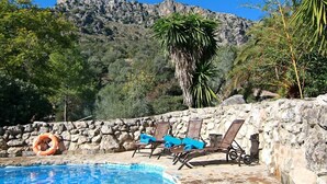 Una piscina amb gandules i un bou salvavides, envoltada per murs de pedra i vegetació, amb un paisatge de muntanyes al fons.