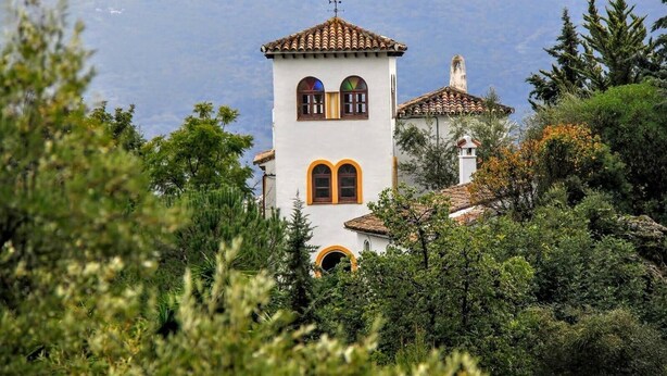 Una torre blanca amb teules vermelles, envoltada de verdura i muntanyes al fons.