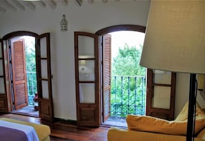 Una habitación con cama, sofá, lámpara y balcón con vista a la vegetación.