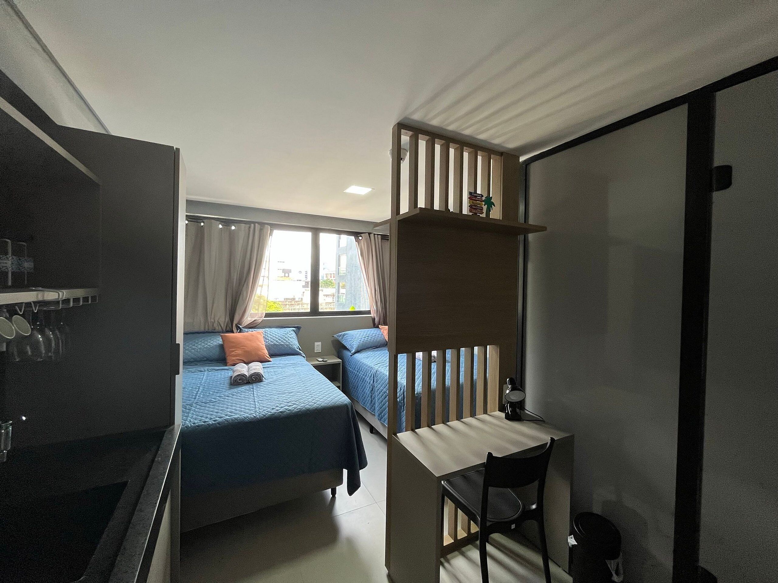 A compact hotel room with two beds, a small desk, and a window with curtains.