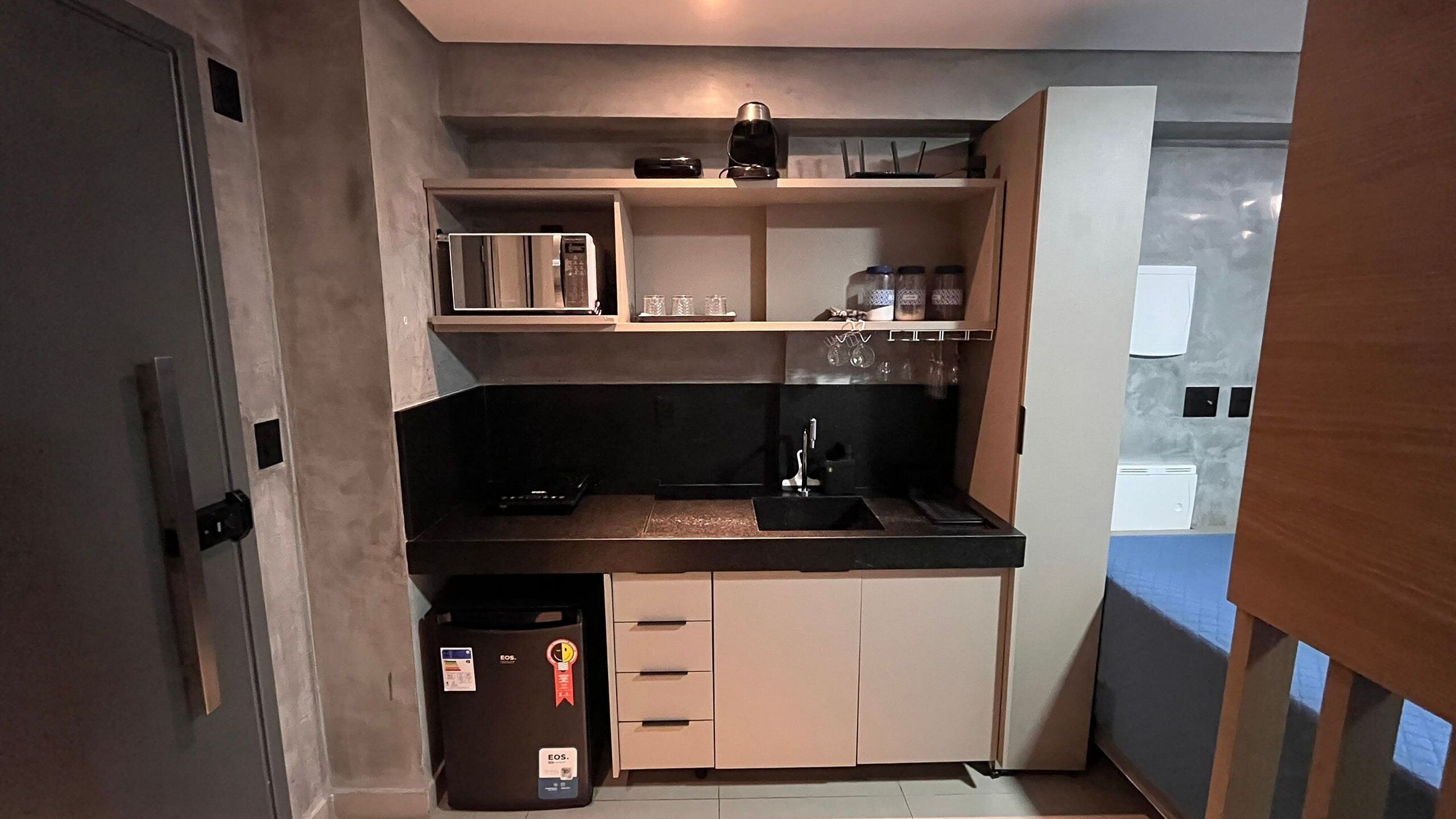 Une cuisine compacte avec un plan de travail noir, un évier et un petit meuble de rangement.