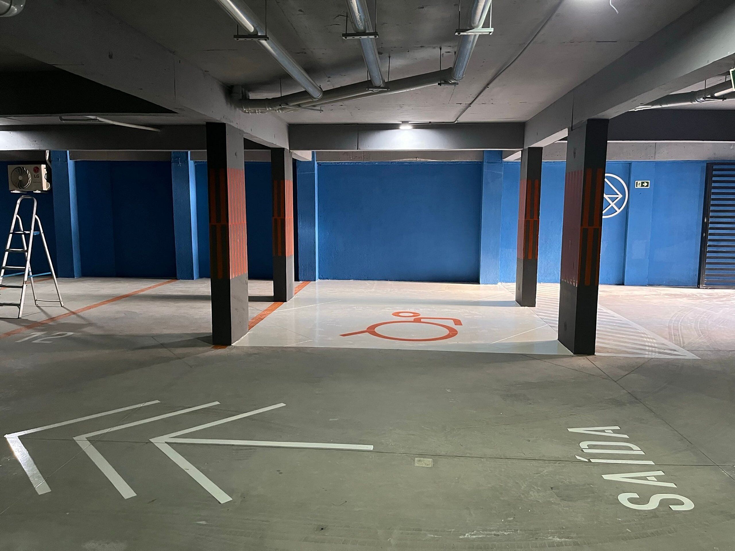 Un parking aux murs bleus, au sol marqué de lignes blanches et doté d’un symbole indiquant qu’il est accessible aux personnes en fauteuil roulant.