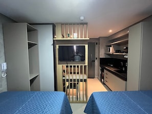 A compact hotel room with two beds, a kitchenette, a small dining area, and a TV mounted on a wall. - Flat Comfort Get One - João Pessoa (João Pessoa)