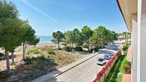 Una carretera costera con coches aparcados, árboles y una playa al fondo.