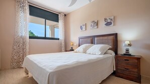 Un dormitorio con una cama grande, una mesita de noche con lámpara y una ventana con cortinas.