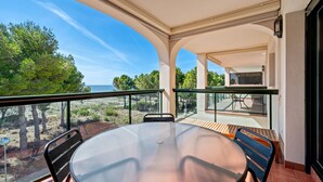 Un balcón con mesa y sillas de vidrio, vista a la playa y un patio con mesa y sillas.