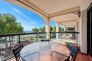 Un balcon avec une table et des chaises en verre, une vue sur la plage et un espace patio avec une table et des chaises.