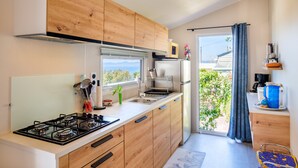 A modern kitchen with wooden cabinets, a gas stove, a sink, and a window with a view of greenery. - Mobil-Home Baia with Sea View and Private Terrace (Saint-Raphaël)