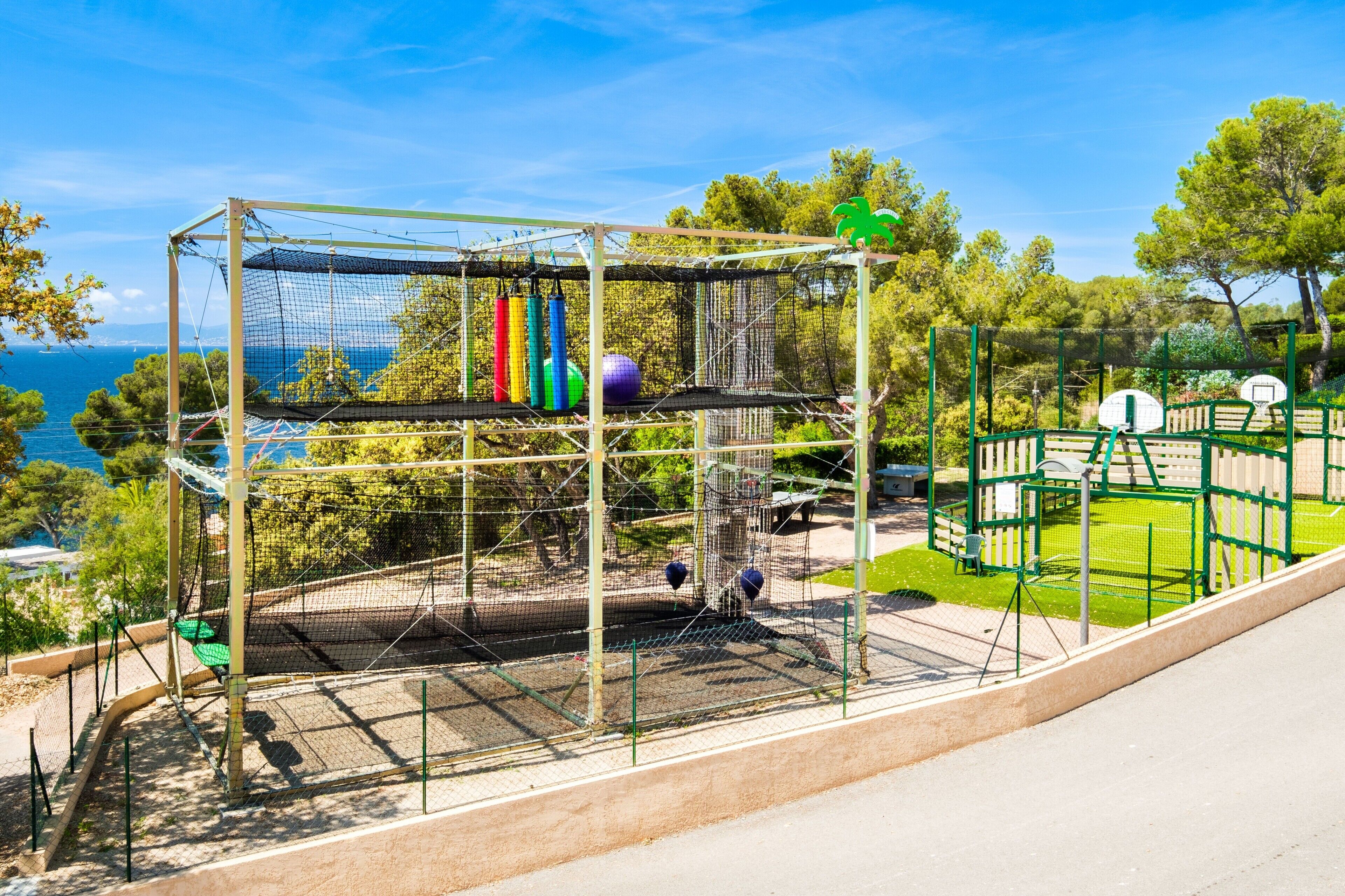 Un parque infantil con una estructura de escalada con red, un aro de baloncesto y vistas al mar.