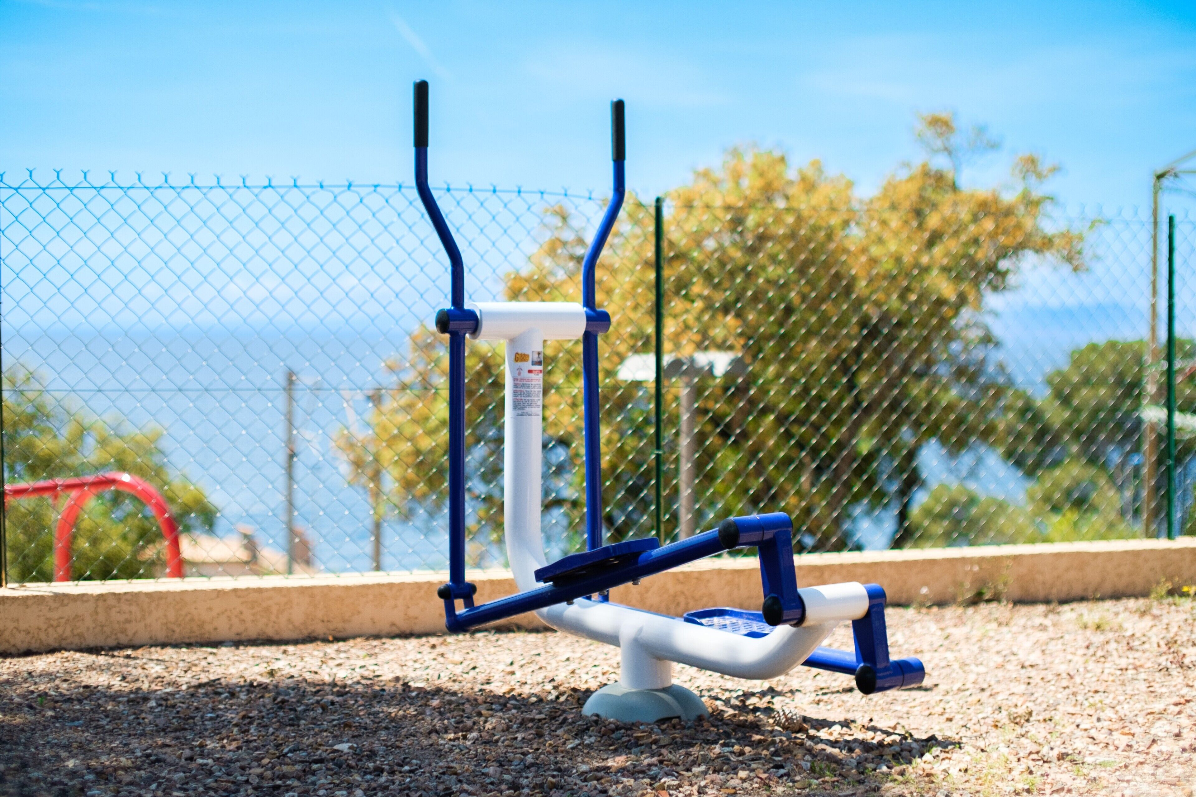 An outdoor exercise machine with a chain-link fence in the background.