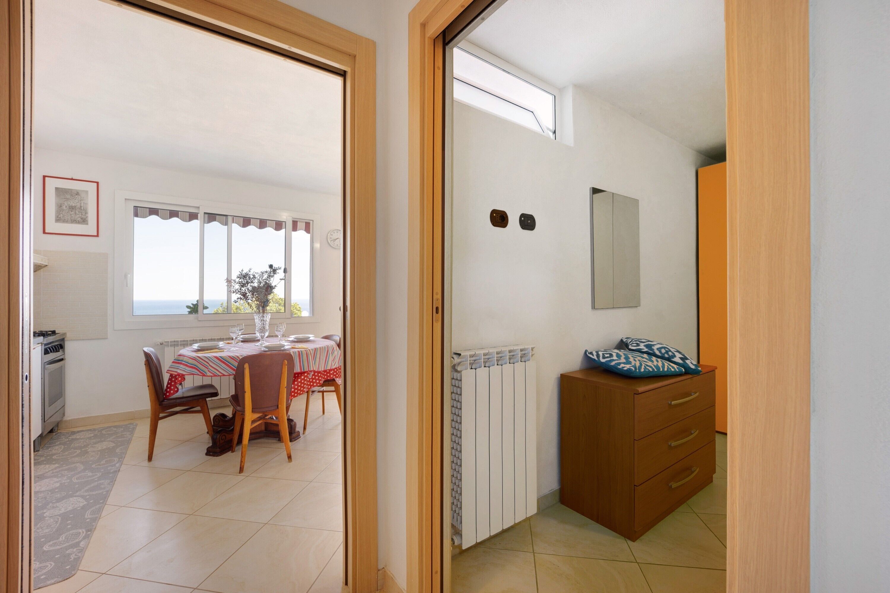 A room with a dining table, chairs, a radiator, a dresser, and a window with a view.