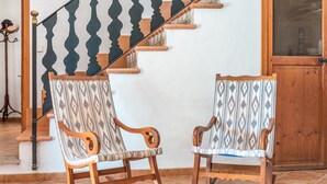 Una scala con gradini in legno e una ringhiera a motivi bianco e nero. Due poltrone a dondolo con rivestimenti decorati sono posizionate su un pavimento piastrellato.