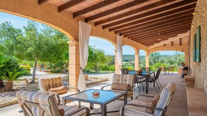 Patio esterno con colonne in pietra, sedute imbottite e un tavolo.