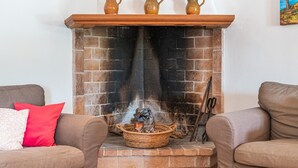 Un caminetto con tre vasi in ceramica sulla mensola, un cesto con legna e un sacco di legna, e un paio di forbici sulla mensola.