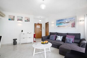 A living room with a grey sofa, a white coffee table, and a painting of a beach scene.