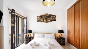 A hotel room with a bed, two bedside tables with lamps, a large wooden wardrobe, and a world map artwork on the wall. - Apartment with Marina and Sea Views – Shared Pool & Wi-Fi (Albufeira)