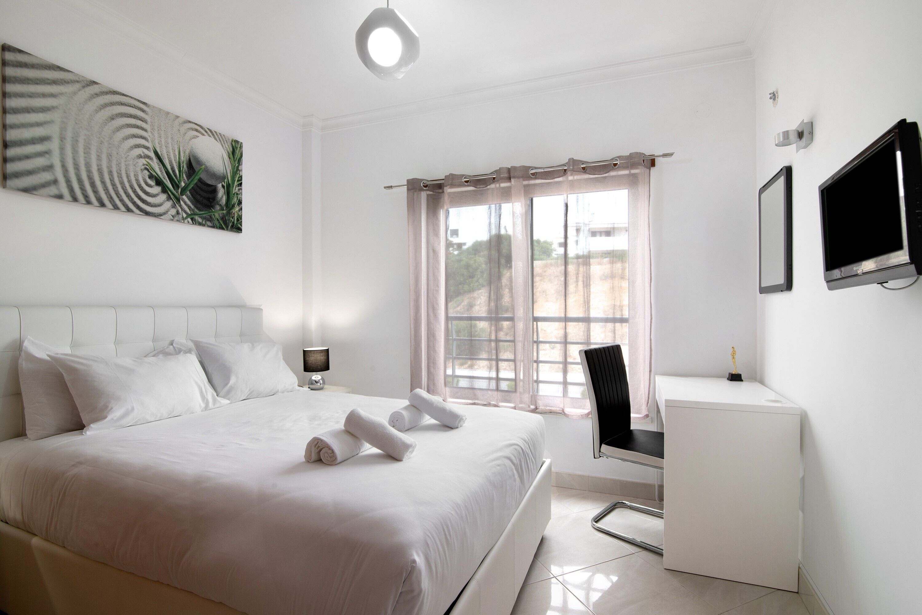 Una habitación de hotel con cama, escritorio, televisor y ventana con cortinas.