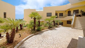 A courtyard with a cobblestone path, palm trees, and a staircase leading to an upper level. - Apartment with Marina and Sea Views – Shared Pool & Wi-Fi (Albufeira)