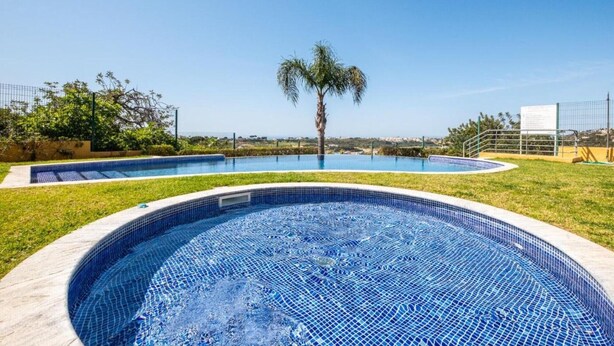 A swimming pool with a palm tree, surrounded by a fence and greenery. - Apartment with Marina and Sea Views – Shared Pool & Wi-Fi (Albufeira)