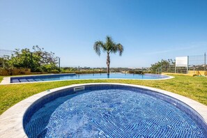 A swimming pool with a palm tree, surrounded by a fence and greenery.