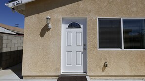 Ein hellbeigees Haus mit Putzfassade, einer weißen Tür, einem Fenster mit Rollläden, einer Überwachungskamera und einem Briefkasten.