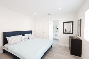A bedroom with a bed, a dresser, a mirror, and a door leading to a bathroom.
