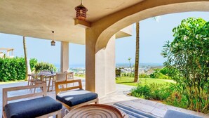 An outdoor patio with a table and chairs, a hanging light fixture, and a view of the landscape. - Apartment "Hacienda Senorio Cifuentes" with Sea View, Shared Pool & Wi-Fi (Benahavis)