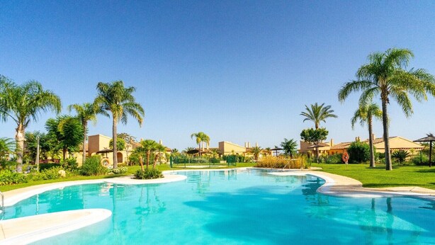 A clear blue pool surrounded by palm trees and buildings. - Apartment "Hacienda Senorio Cifuentes" with Sea View, Shared Pool & Wi-Fi (Benahavis)