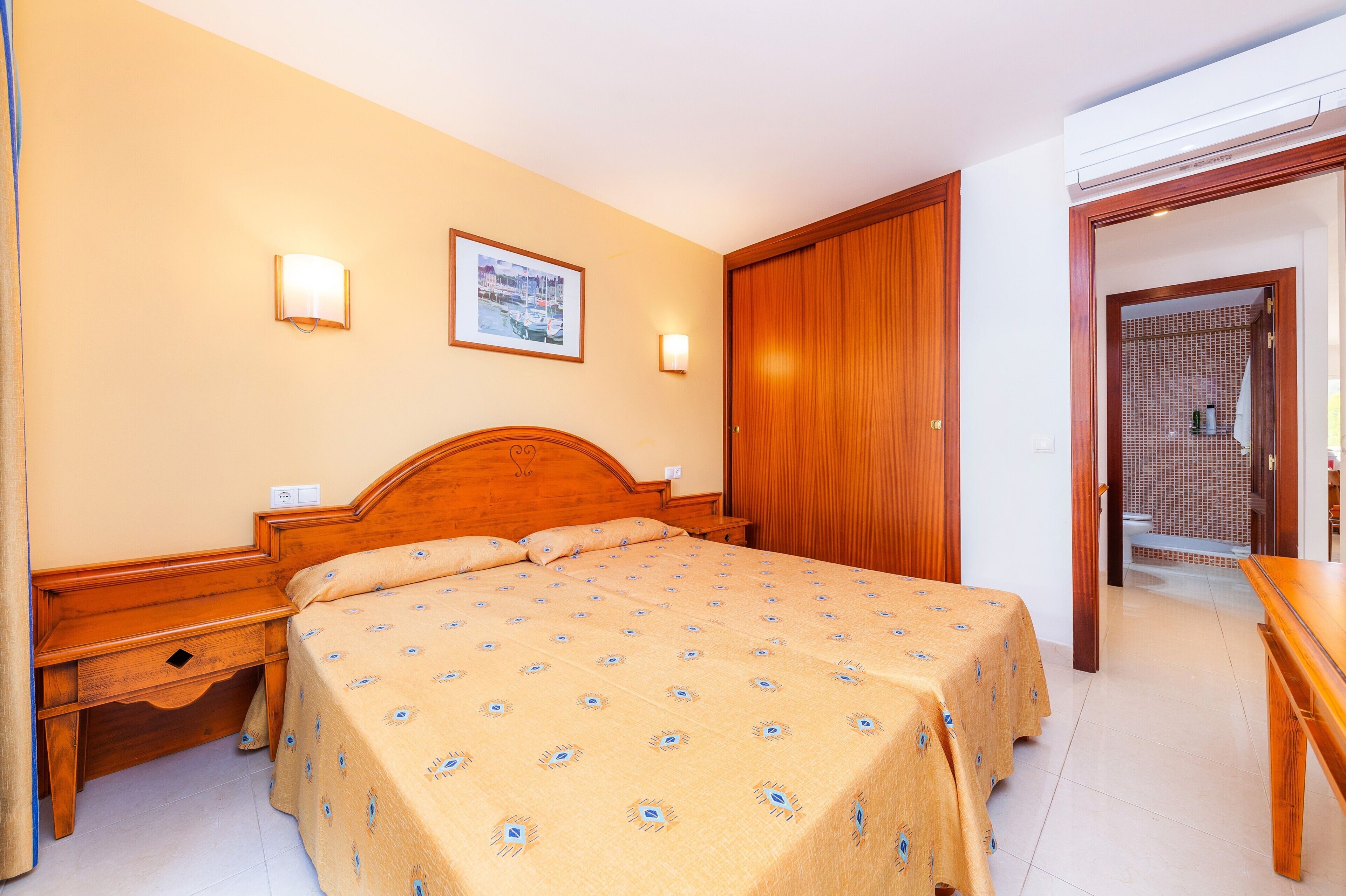 A hotel room with a wooden bed, bedside tables, a wall-mounted picture, and a door leading to a bathroom.