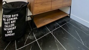 Un baño con tocador de madera, dos espejos, una planta y un cubo de basura con una frase motivadora.